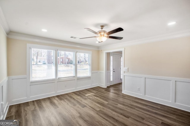 spare room featuring ceiling fan, a wainscoted wall, dark wood-style flooring, visible vents, and crown molding