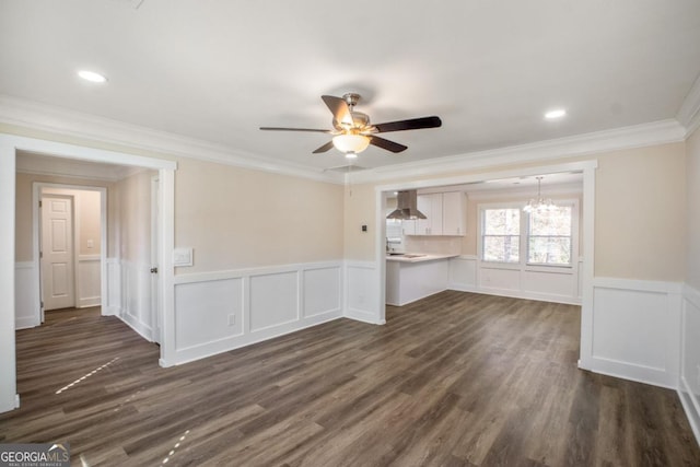 unfurnished living room featuring a wainscoted wall, recessed lighting, dark wood-type flooring, ornamental molding, and ceiling fan with notable chandelier