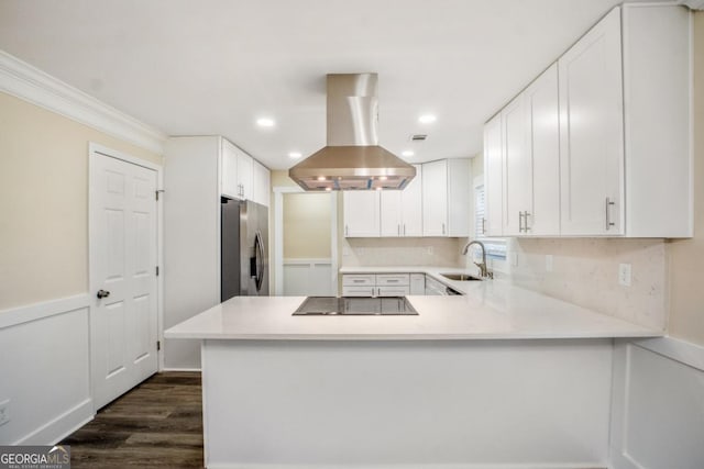 kitchen with black electric cooktop, island range hood, a peninsula, light countertops, and stainless steel refrigerator with ice dispenser