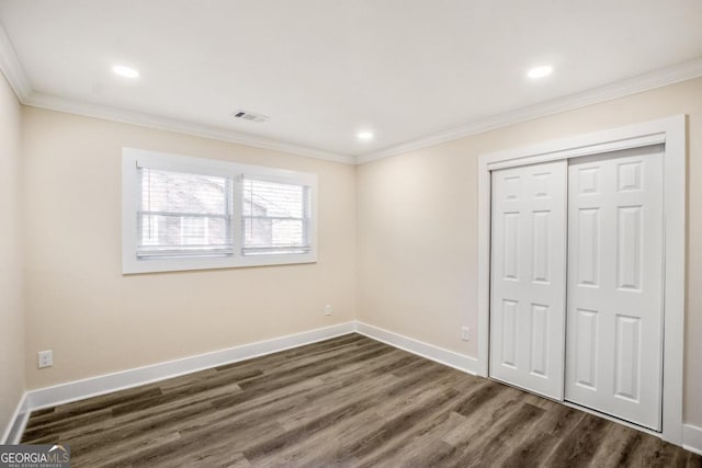 unfurnished bedroom featuring dark wood-style flooring, visible vents, baseboards, ornamental molding, and a closet