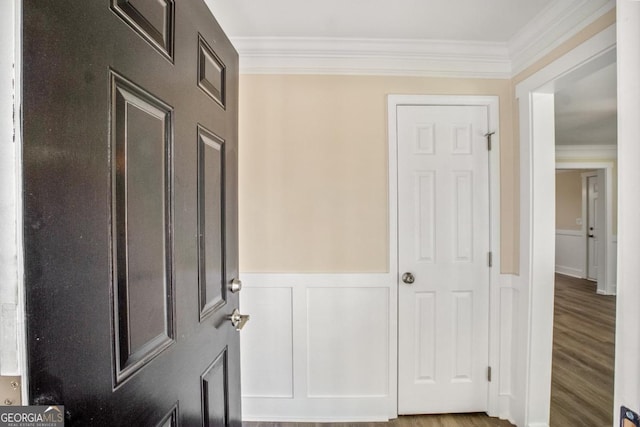 interior space with a wainscoted wall, crown molding, a decorative wall, and wood finished floors