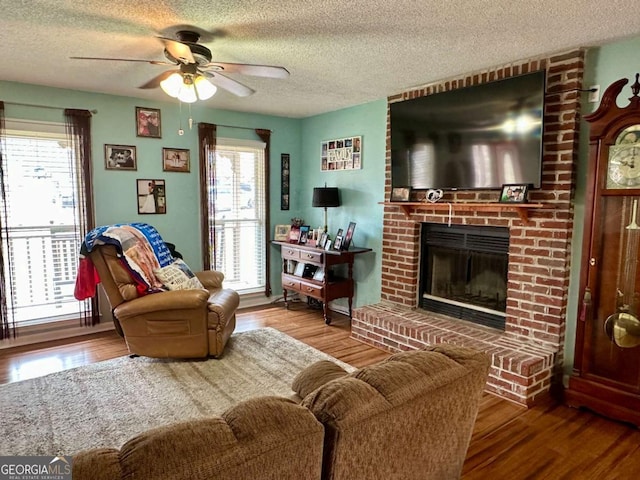 living room featuring a textured ceiling, ceiling fan, a fireplace, and wood finished floors