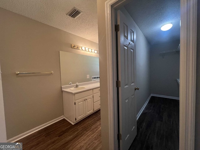 bathroom featuring visible vents, vanity, a textured ceiling, wood finished floors, and baseboards