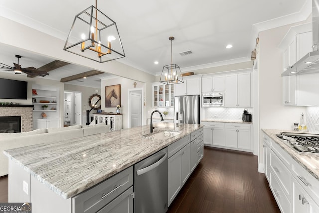 kitchen featuring wall chimney range hood, white cabinets, visible vents, stainless steel appliances, and a sink