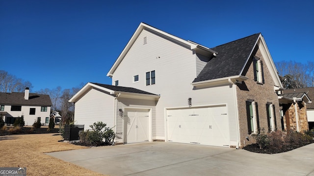 view of side of property featuring brick siding, driveway, a garage, and roof with shingles