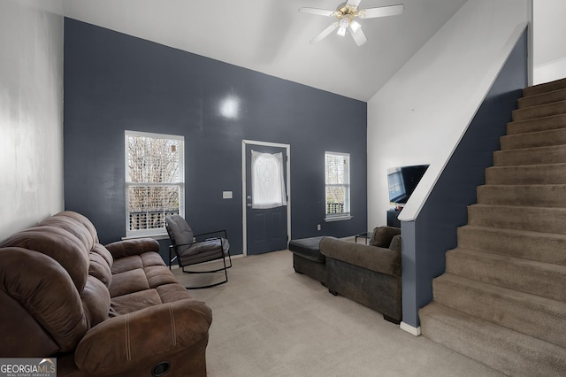 living room featuring baseboards, light colored carpet, ceiling fan, stairway, and high vaulted ceiling