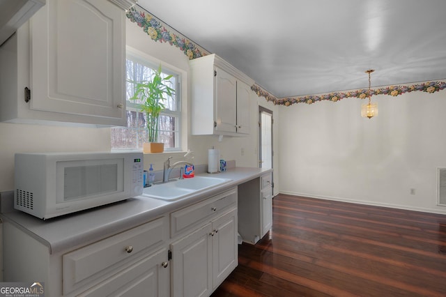 kitchen featuring white microwave, dark wood-style floors, light countertops, white cabinetry, and a sink