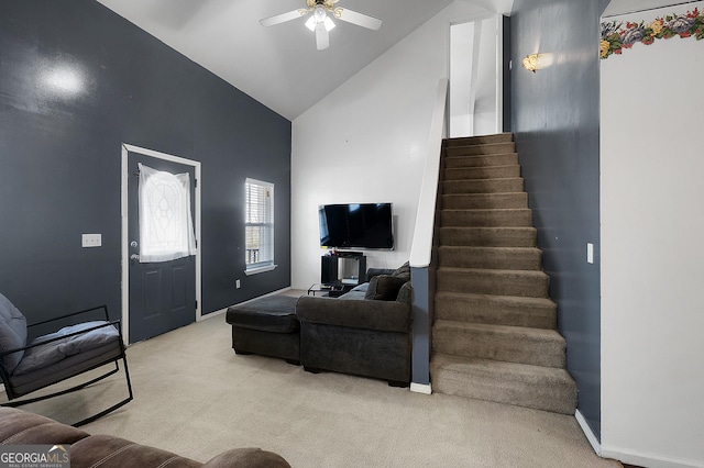 living area featuring baseboards, a ceiling fan, light colored carpet, stairs, and high vaulted ceiling