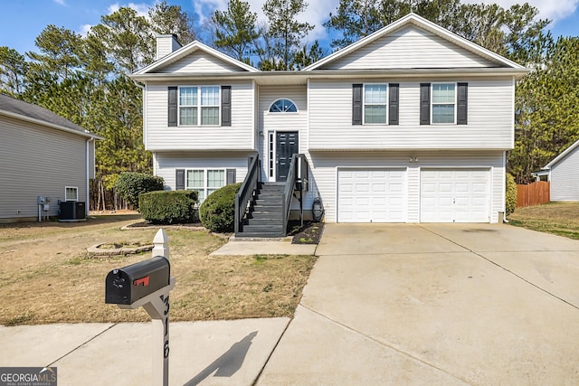 split foyer home featuring a chimney, an attached garage, central AC unit, driveway, and a front lawn