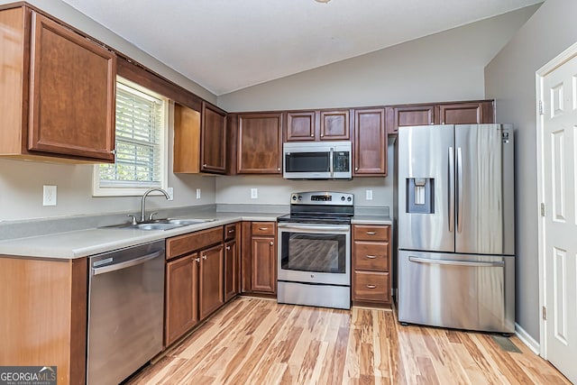 kitchen with light wood-style flooring, stainless steel appliances, a sink, vaulted ceiling, and light countertops