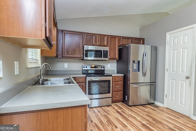 kitchen with vaulted ceiling, light countertops, appliances with stainless steel finishes, and a sink