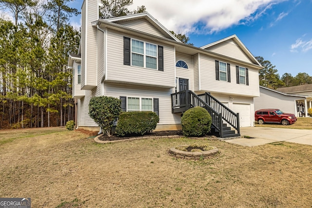 raised ranch featuring a garage, driveway, a chimney, and a front lawn