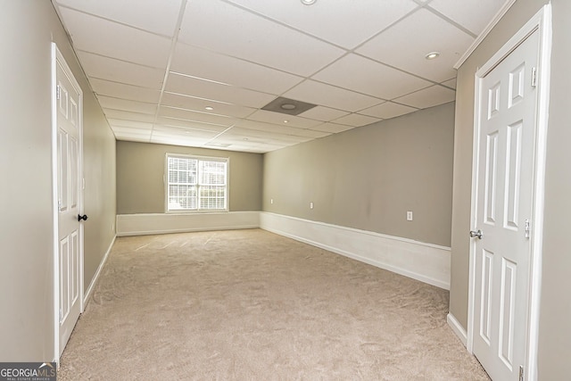 spare room with baseboards, a drop ceiling, and light colored carpet