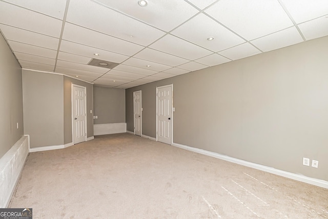 empty room featuring light carpet, a drop ceiling, and baseboards