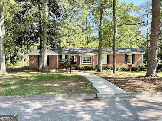 ranch-style house featuring a chimney, a front lawn, and brick siding