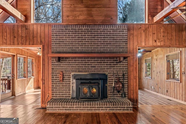 unfurnished living room with plenty of natural light, wooden walls, a high ceiling, and wood finished floors