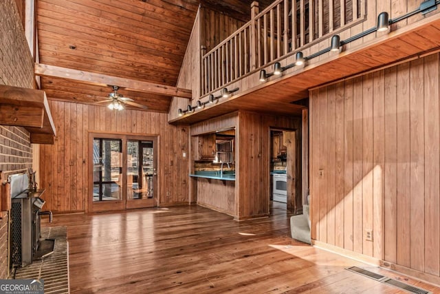 unfurnished living room featuring wooden walls, ceiling fan, wood finished floors, a wood stove, and high vaulted ceiling