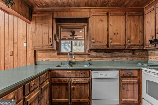 kitchen with wooden ceiling, wooden walls, white appliances, a sink, and dark countertops