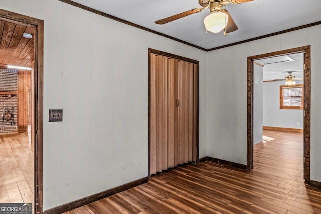 spare room featuring baseboards, ornamental molding, ceiling fan, and dark wood-type flooring