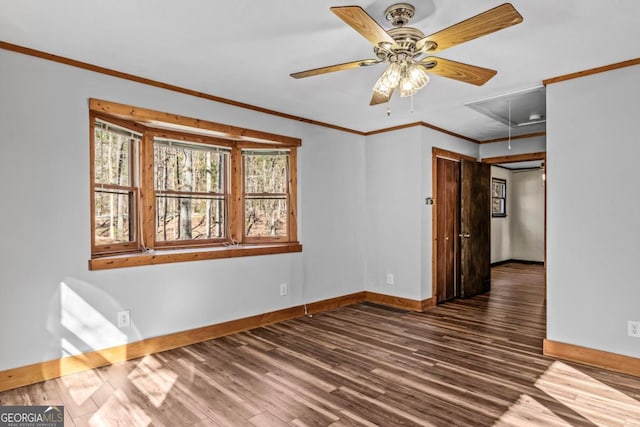 unfurnished room featuring attic access, baseboards, ceiling fan, dark wood-type flooring, and crown molding