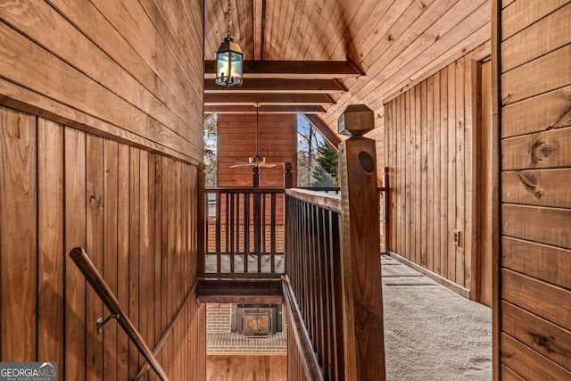 stairway featuring wooden ceiling, carpet floors, wood walls, a ceiling fan, and beam ceiling