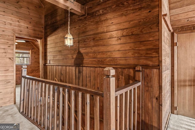 interior space with light carpet, beamed ceiling, wood walls, and an upstairs landing