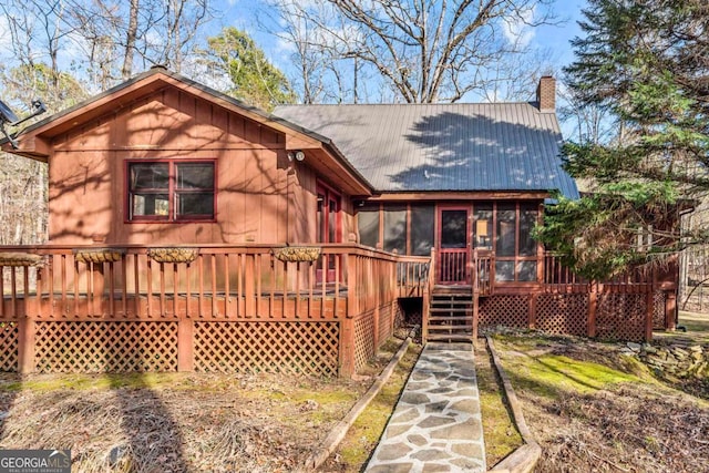 back of house with a sunroom, metal roof, a chimney, and a wooden deck