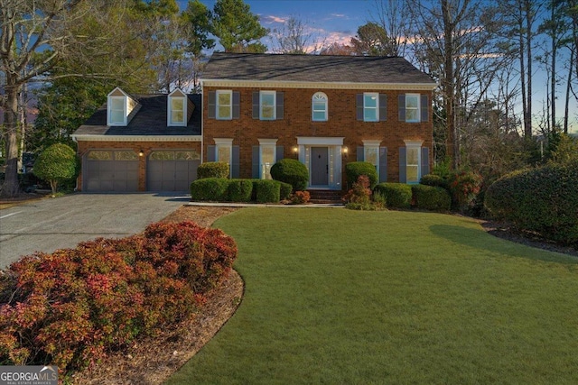 colonial-style house with an attached garage, driveway, a lawn, and brick siding