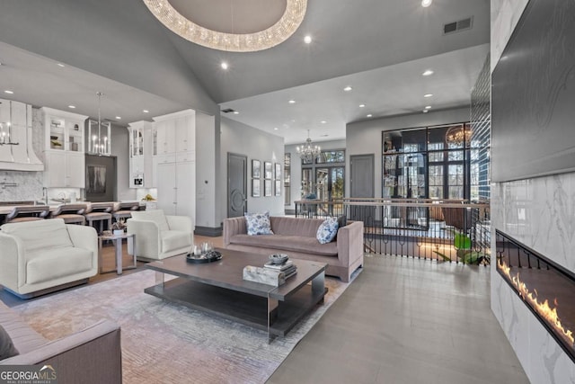 living area featuring a chandelier, high vaulted ceiling, recessed lighting, visible vents, and a glass covered fireplace