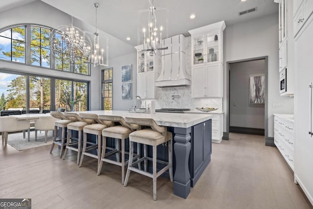 kitchen featuring glass insert cabinets, white cabinets, custom range hood, and a center island with sink