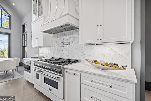 kitchen with range with two ovens, white cabinetry, glass insert cabinets, and custom range hood