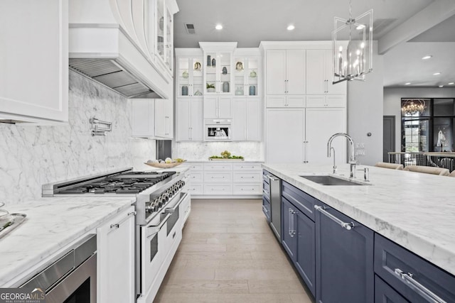 kitchen featuring blue cabinets, stainless steel appliances, white cabinets, custom exhaust hood, and glass insert cabinets