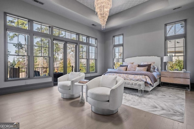 bedroom featuring a raised ceiling, wood finished floors, visible vents, and an inviting chandelier