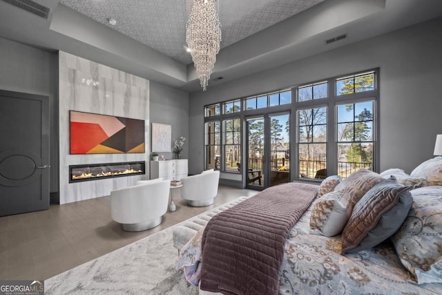 bedroom with a fireplace, visible vents, access to exterior, a raised ceiling, and an inviting chandelier