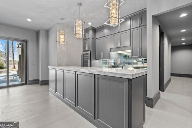 kitchen featuring tasteful backsplash, light stone countertops, decorative light fixtures, and gray cabinetry