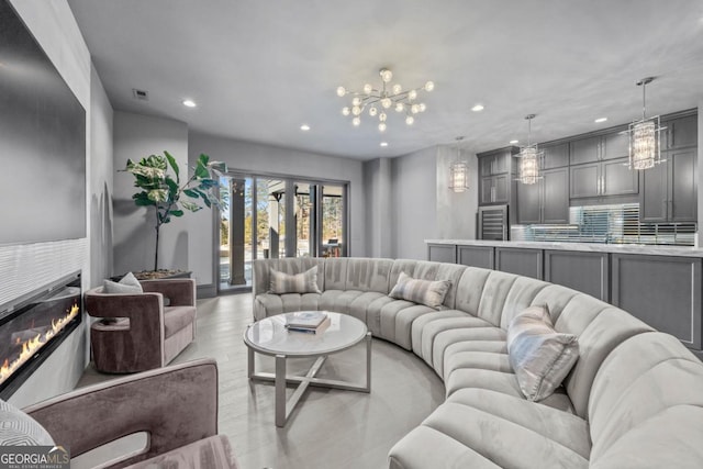 living room featuring visible vents, a glass covered fireplace, light wood-style flooring, a notable chandelier, and recessed lighting