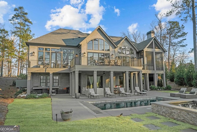 rear view of house with an outdoor pool, a lawn, a patio, a balcony, and a chimney