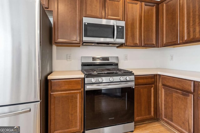 kitchen with stainless steel appliances, brown cabinetry, light countertops, and light wood-style flooring