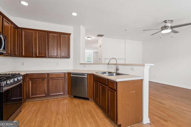 kitchen featuring light wood-style flooring, a peninsula, stainless steel appliances, light countertops, and a sink