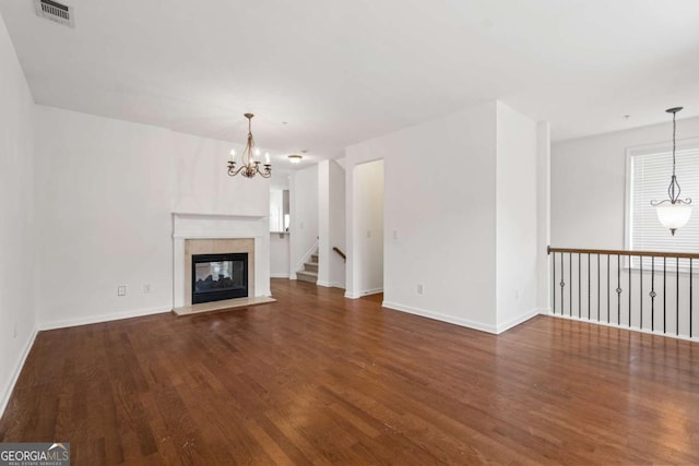 unfurnished living room with a chandelier, a tile fireplace, visible vents, baseboards, and dark wood finished floors