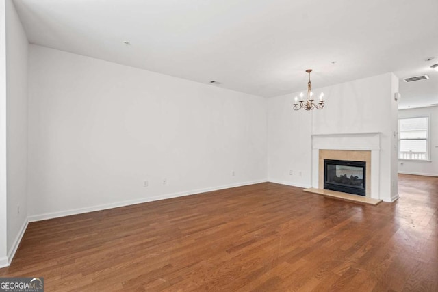 unfurnished living room featuring visible vents, dark wood-type flooring, a glass covered fireplace, a chandelier, and baseboards