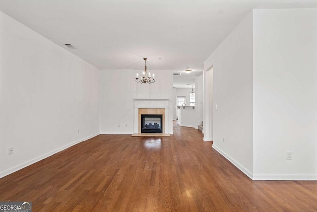 unfurnished living room with baseboards, visible vents, wood finished floors, an inviting chandelier, and a multi sided fireplace