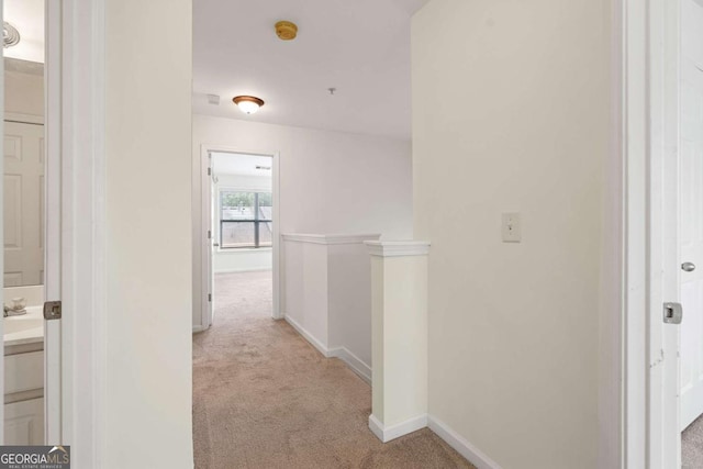 hall with light carpet, baseboards, and an upstairs landing