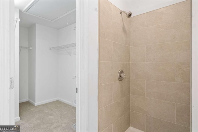 bathroom with a spacious closet, baseboards, and tiled shower