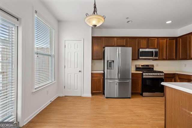 kitchen with stainless steel appliances, light countertops, light wood finished floors, brown cabinetry, and pendant lighting