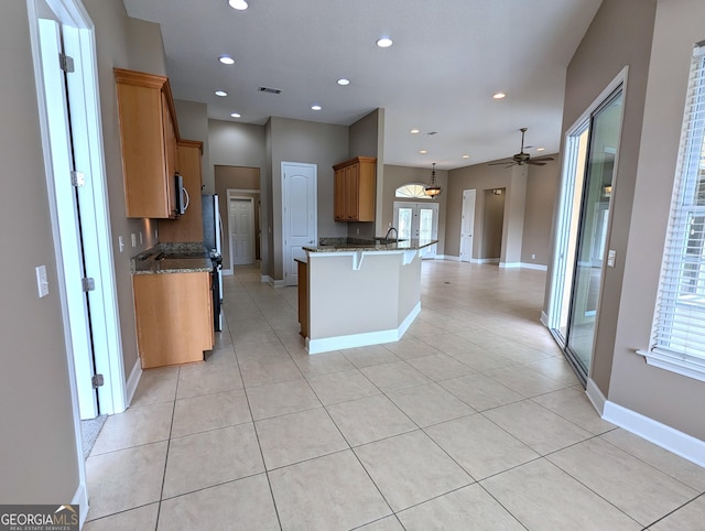 kitchen with brown cabinets, a breakfast bar area, visible vents, dark stone counters, and a peninsula