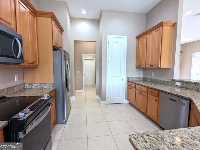 kitchen with brown cabinets, light stone countertops, light tile patterned floors, and stainless steel appliances