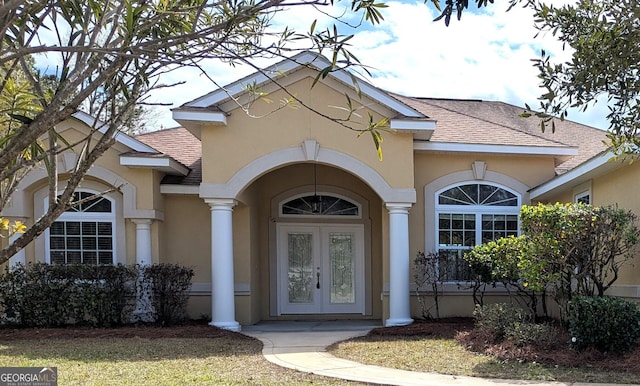 property entrance featuring stucco siding, a shingled roof, and french doors