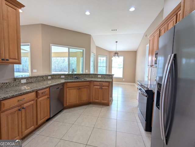 kitchen with light tile patterned floors, stainless steel appliances, a sink, brown cabinetry, and dark stone countertops