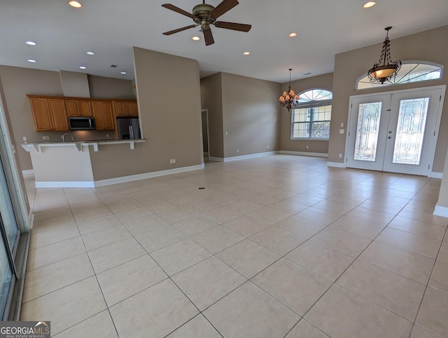 unfurnished living room with ceiling fan with notable chandelier, baseboards, french doors, and recessed lighting